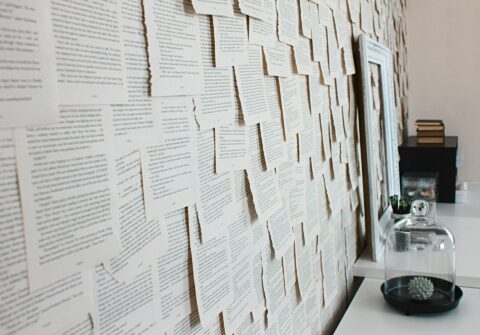 Foto einer Wand mit einzelnen herausgerissenen Buchseiten vor einem Tisch mit Dekoelementen