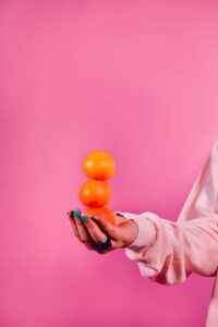 Eine Hand balanciert drei Orangen vor pinkem Hintergrund